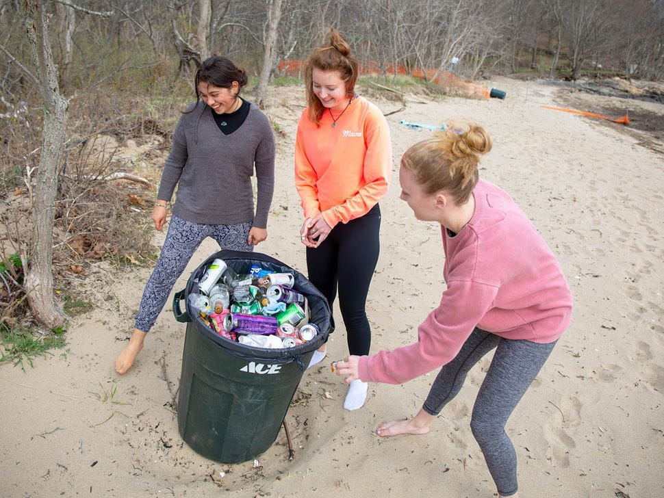 hree Endicott  students cleaning up waste at the beach near Tupper Hall