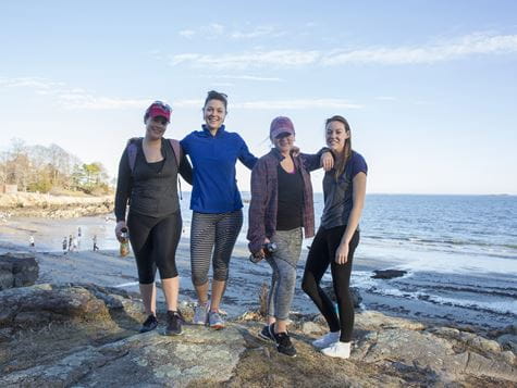 four people standing on rocks on endicott beach with ocean behind them