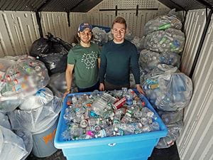 Two Endicott students standing behind a large container filled with cans to be recycled