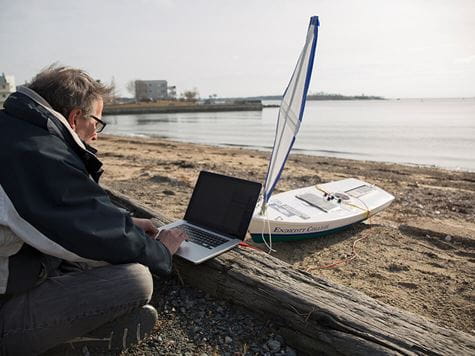 professor working on solar powered boat on laptop on endicott beach