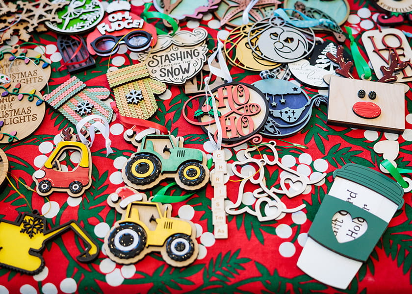 High-angle close-up of festive wooden Christmas ornaments and cutout decorations arranged on a patterned red cloth.