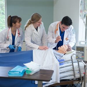 two nursing students practicing on a dummy with their teacher supervising