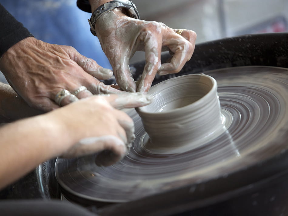 close up shot of two people working on a clay piece on potter's wheel