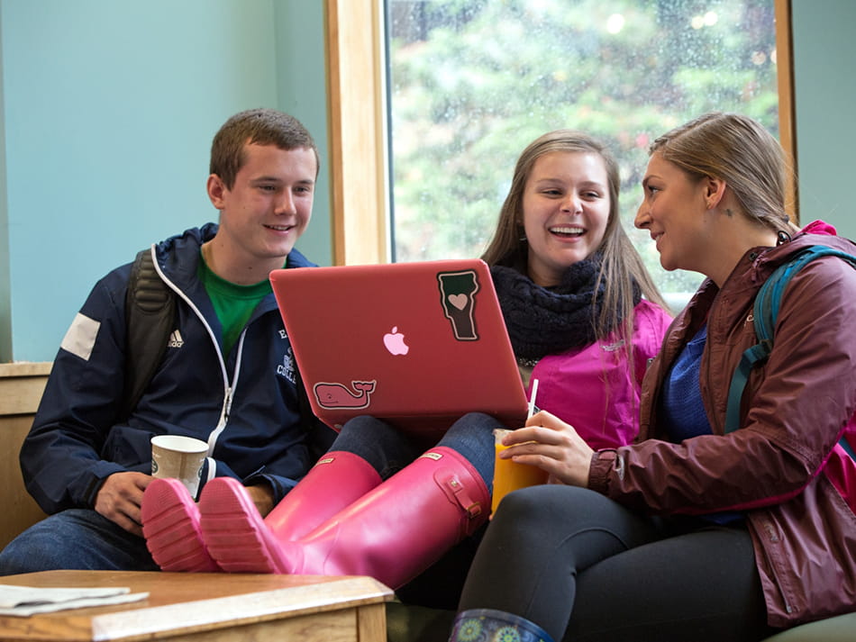 three students socializing and working on laptop in lounge area