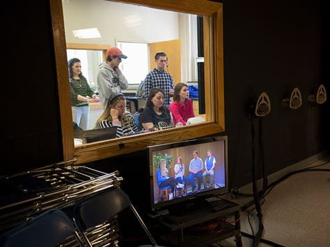 communications students monitoring a live broadcast from behind a window