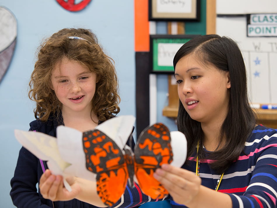 a kid showing off two butterfly drawings for an elementary education teacher