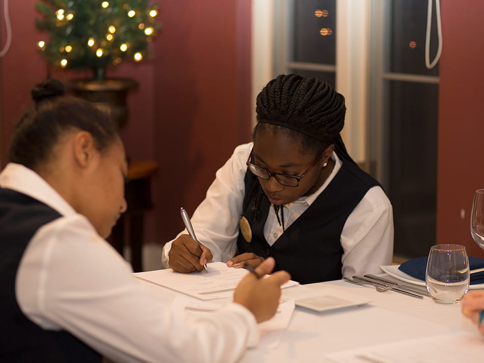 two hospitality management students writing in a book