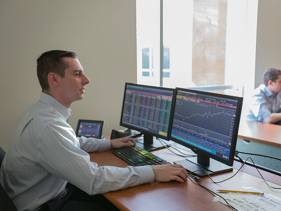 a business student monitoring the stock market on two computer monitors