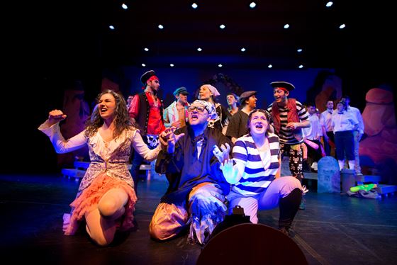 group of students gathered on stage during performance taking a knee towards crowd