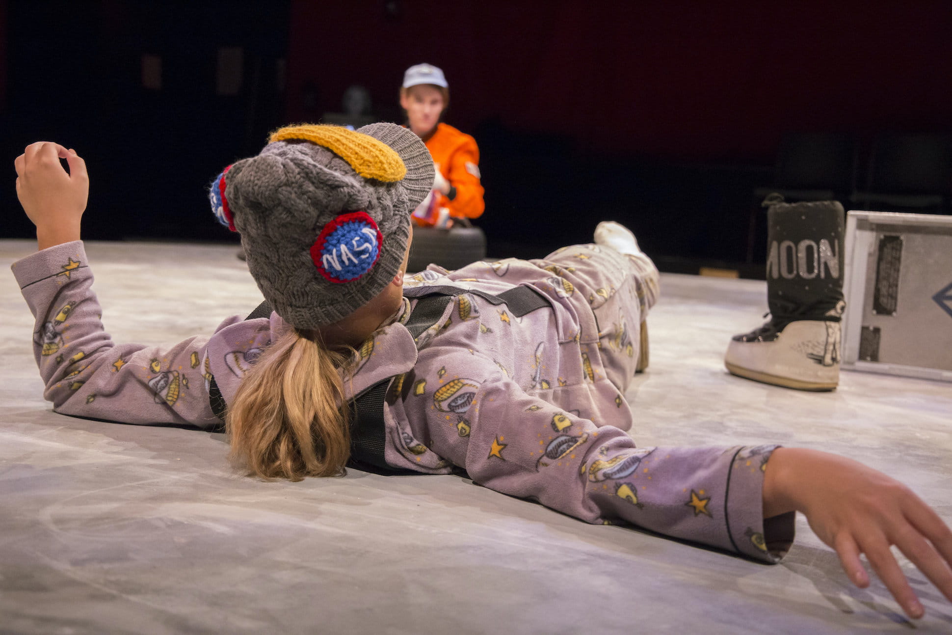 actor lays on floor in costume with beanie hat with nasa button on top