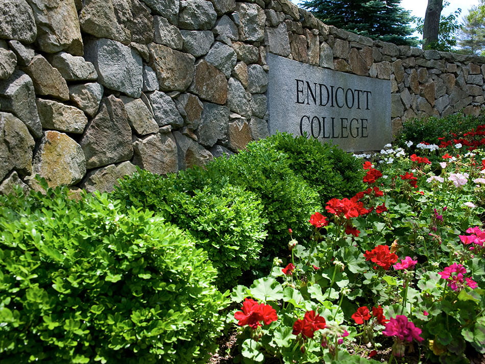 angled shot of stone sign for endicott college surrounded by flowers