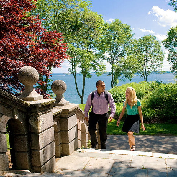 Two students walking up stairs behind College Hall with ocean in the background