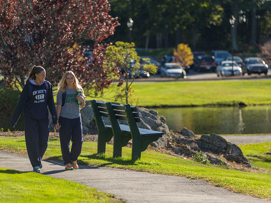 two students talking and walking down path next to pond on campus