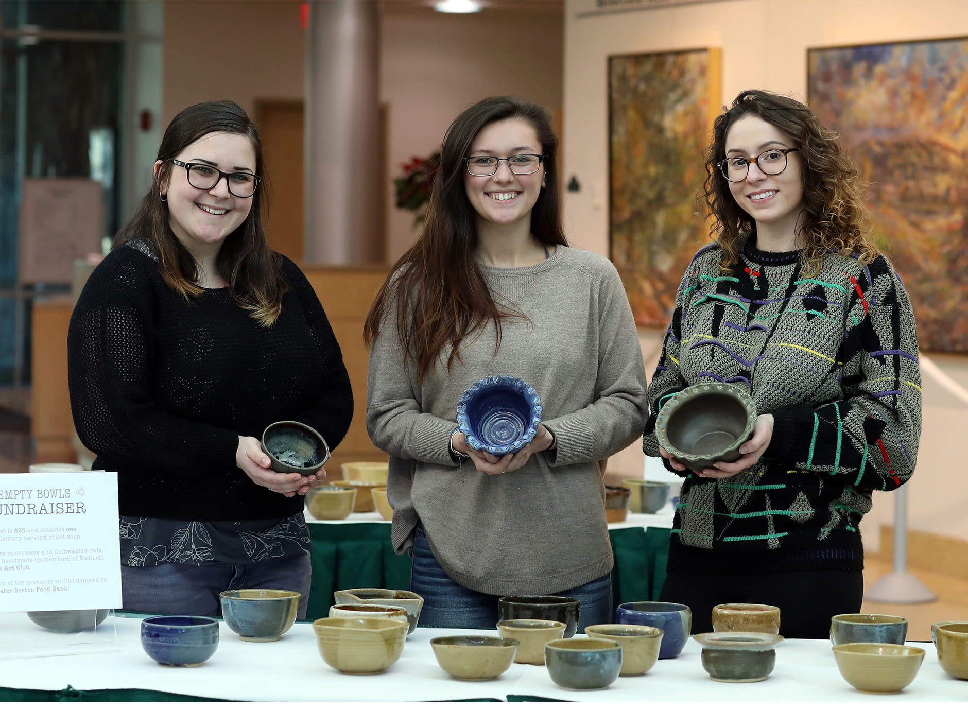 Students hold handmade ceramic bowls at the Empty Bowls Fundraiser in the Walter J. Manninen Center for the Arts atrium