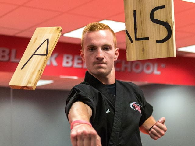 Rob Ackerman breaking through a wooden board marked with the letters ALS 