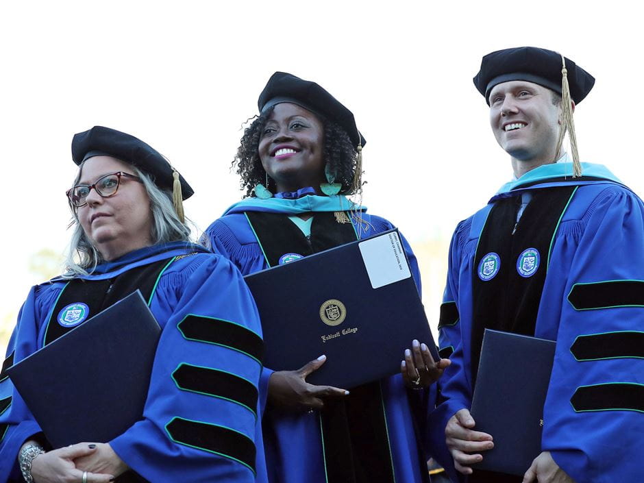 three doctoral graduates pose at commencement with their diplomas 