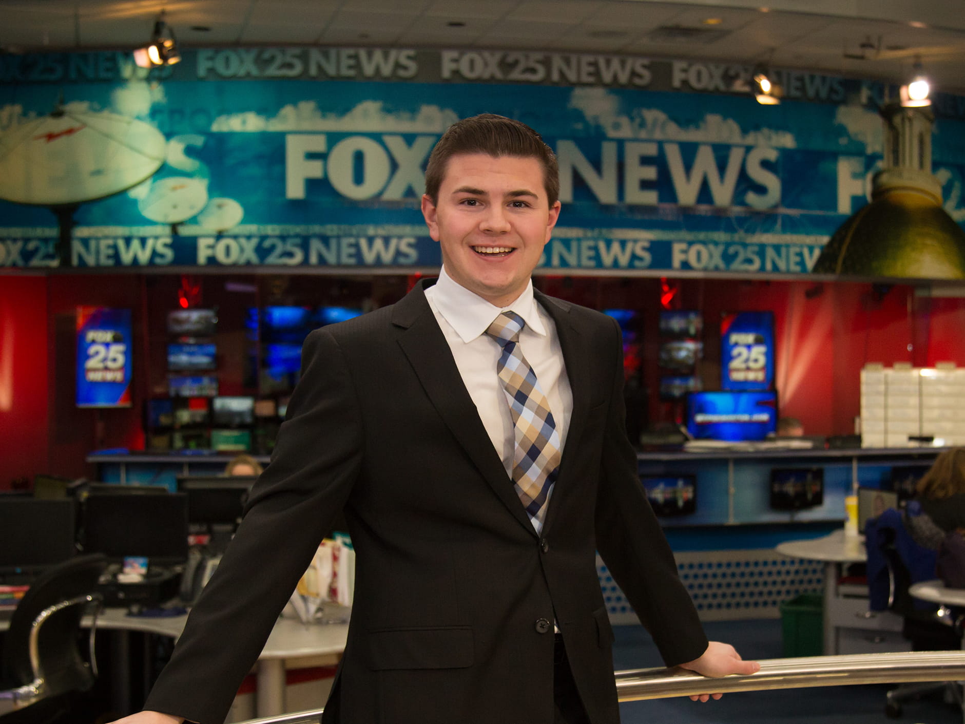 Male student pictured in front of the Fox25 newsroom while on internship.