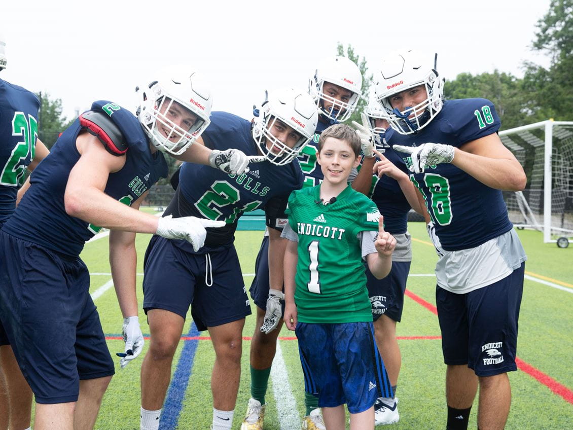 Team IMPACT participant Erik Bell poses with members of the Endicott College Football team