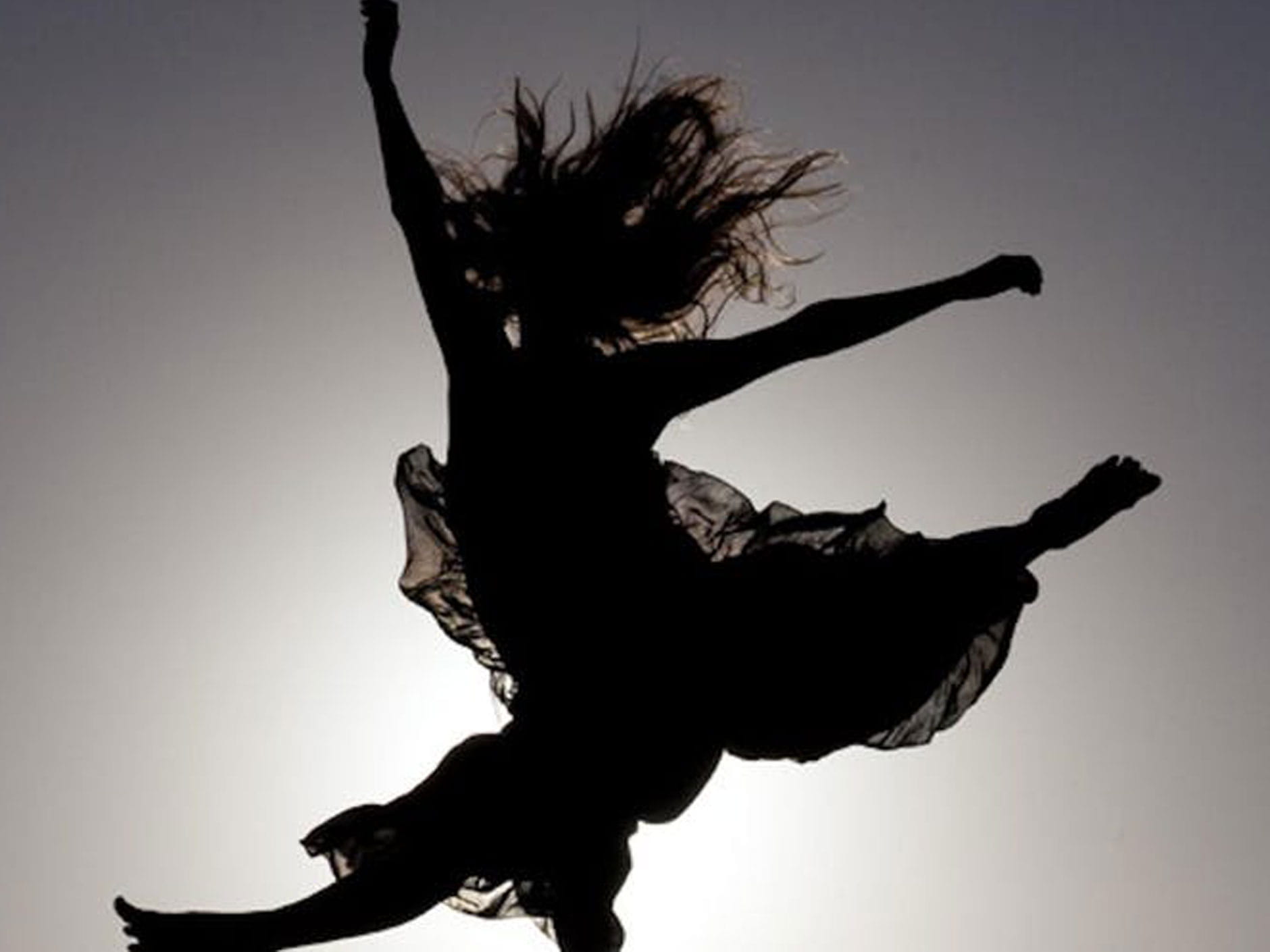 A backlit silhouette of a dancer leaping through the air 