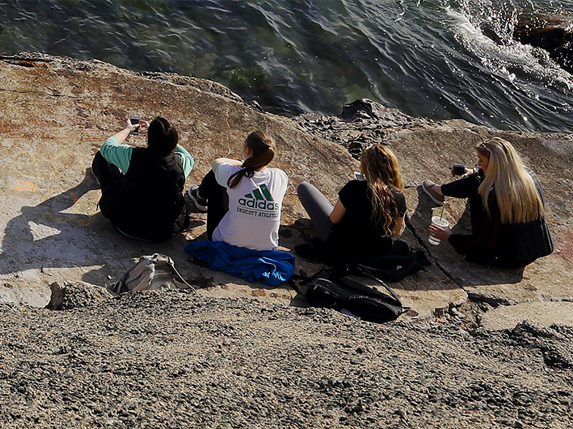 Four students sitting at Peace Rock next to the Atlantic ocean