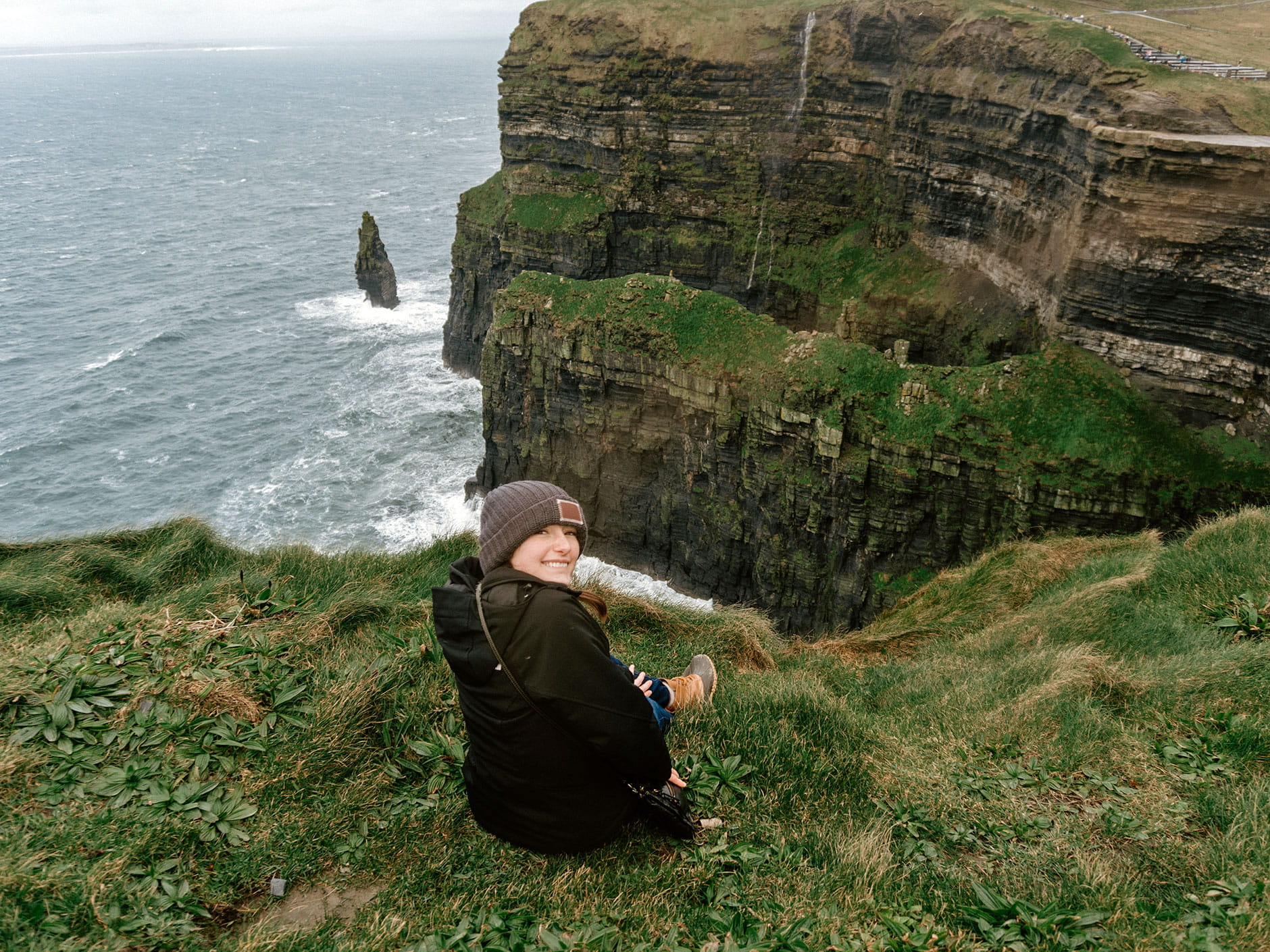Female student sitting on the Cliffs of Moher smiling back at the camera