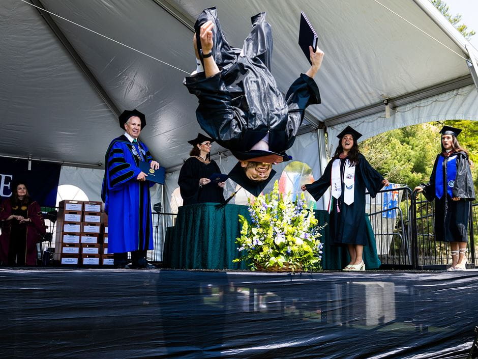 A student jumps off stage after receiving his degree