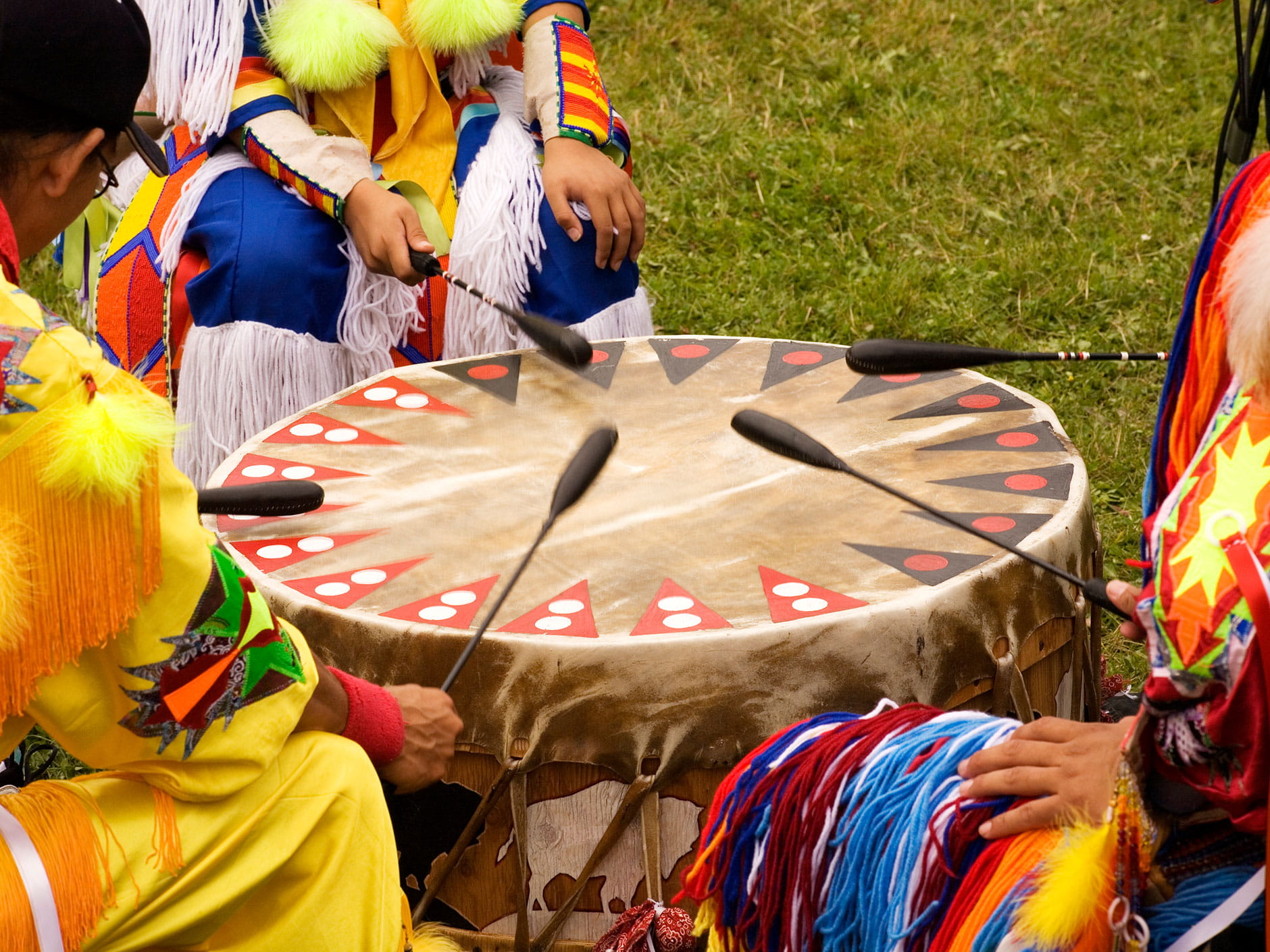 Several people play a large traditional drum outdoors