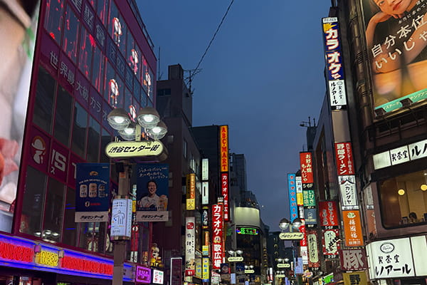 A Tokyo city street in Shibuya at dusk, filled with bright neon signs and buildings.