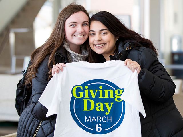 Two Endicott students holding up a shirt displaying the Giving Day March 6 t-shirt