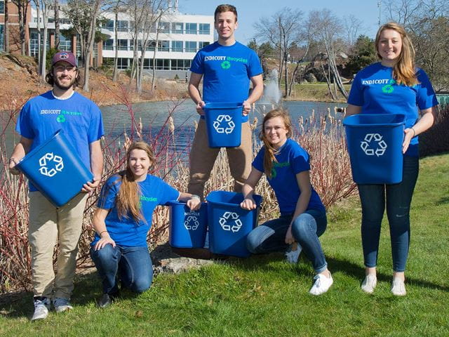 Students hold recycling bins outside a pond at Endicott College