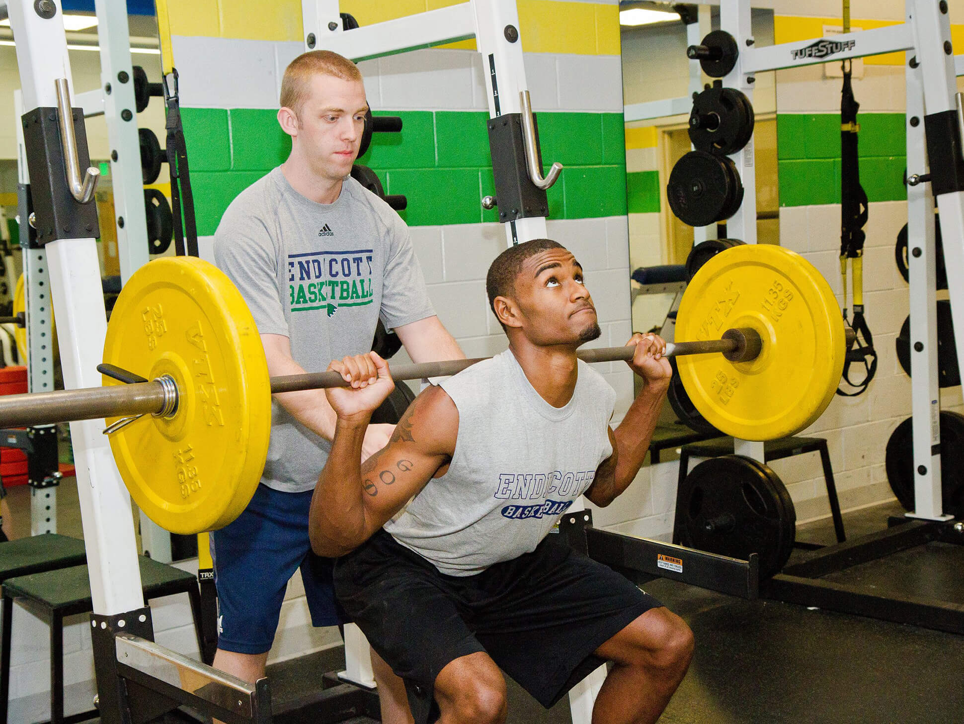 student lifting weights in fitness center with friend spotting his lifting