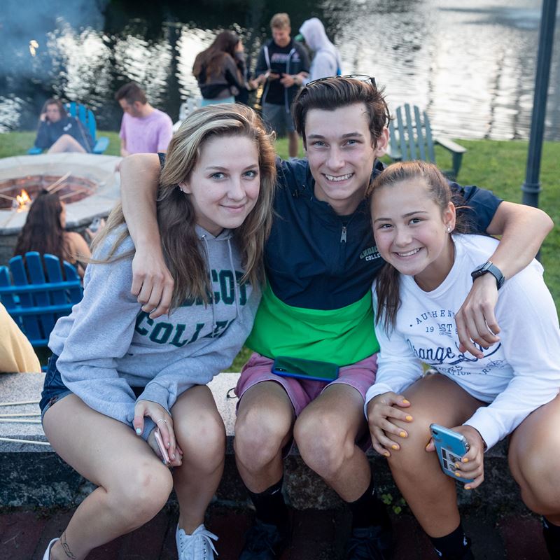 Three students hug and smile near the Endicott Lakes at summer orientation