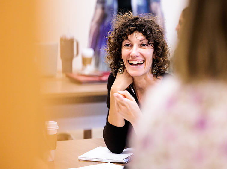 A smiling woman with curly dark hair engaging in a discussion during a meeting or class.