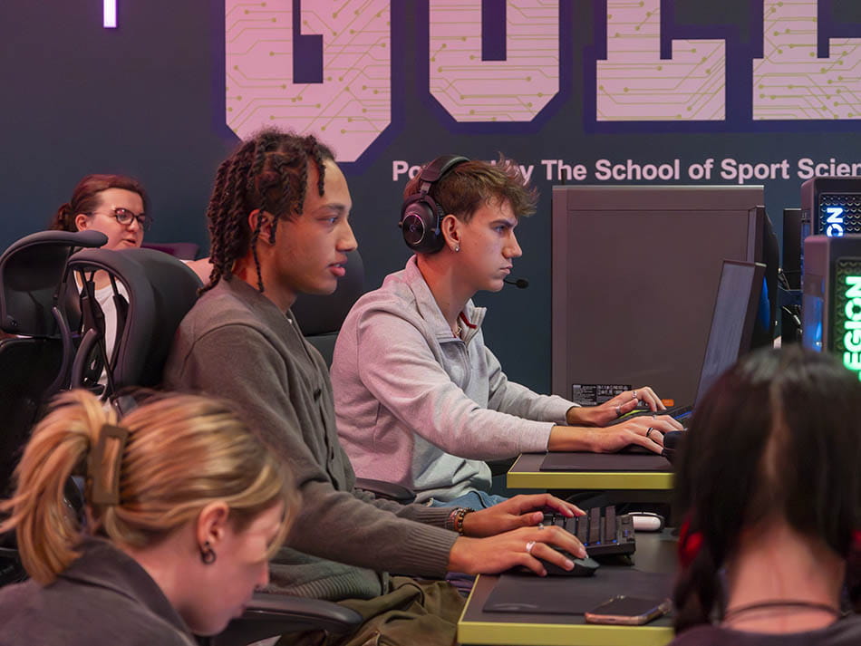 Students wearing headsets seated at computer stations in an esports gaming room.
