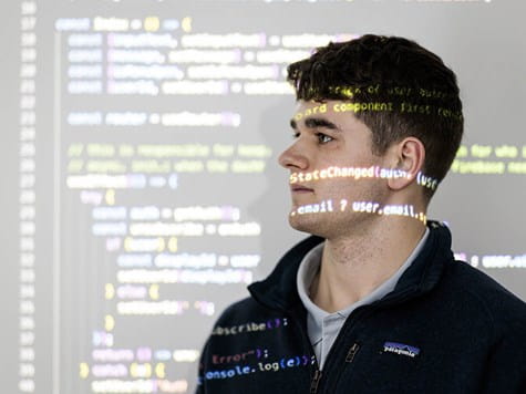 A young man looking forward with computer code projected across his face and background.