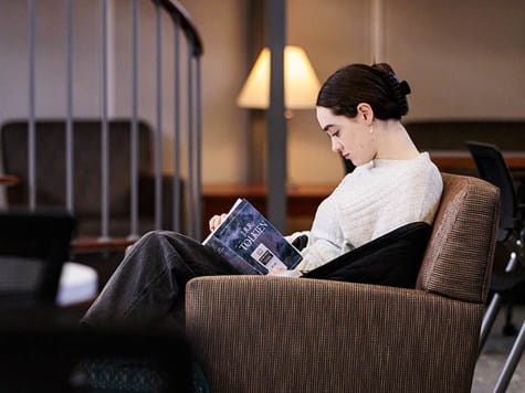 A female student curled up in an armchair intently reading a book.